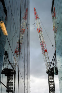 Low angle view of cranes against sky in city