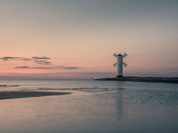 Windmill by sea against sky during sunset