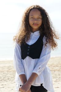 Portrait of young woman standing at beach against sky on sunny day