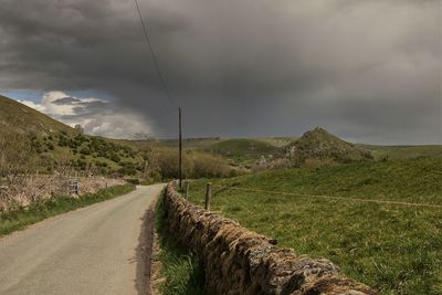 Empty road amidst field against sky