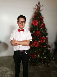Portrait of smiling young man standing by christmas tree at home