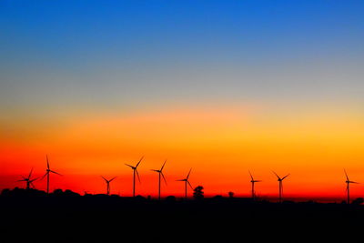 Silhouette wind turbines on field against sky during sunset