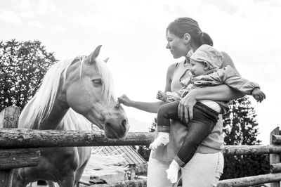 Mother touching horse while carrying daughter