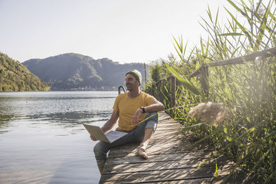 Mature man with laptop on jetty looking at lake view