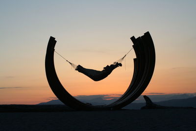 Silhouette child in hammock against sky during sunset