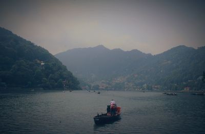 Boat sailing on river by mountains against sky