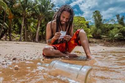 Man drinking water while sitting on land against trees