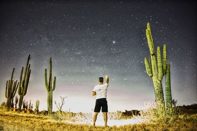 Rear view of man standing on field against sky at night