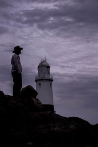 Side view of man standing on rocks with lighthouse in background