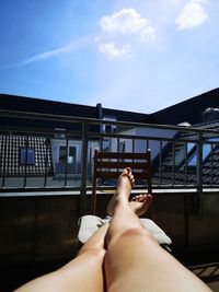 Low section of person relaxing on building against sky