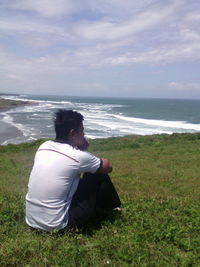 Man sitting on beach looking at sea against sky