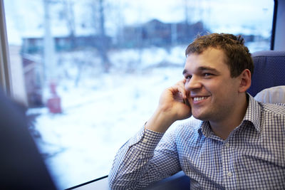 Smiling young businessman talking on phone in train