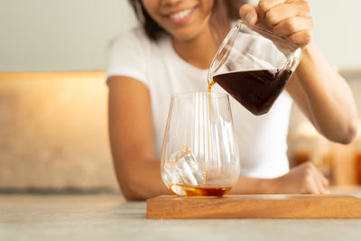 Happy woman pouring cold brew coffee into glass with iced on table.