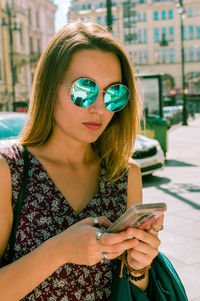 Young stylish woman in glasses stands on the street and looks at the phone. vintage tones.