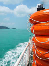 Stack of orange inflatable rings on boat deck in sea against sky