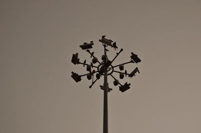 Low angle view of birds perching on floodlight against clear sky