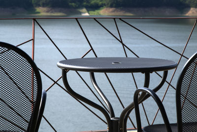 Empty chairs and table by swimming pool against lake