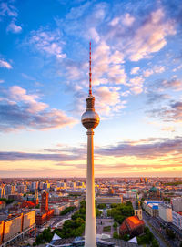 Communications tower in city against sky during sunset