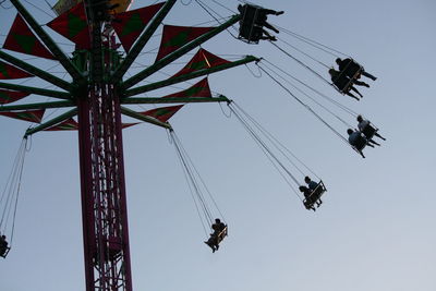 Low angle view of people on chain swing ride against clear sky