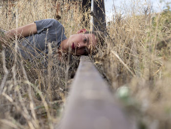 Portrait of man resting on abandoned railroad track on grassy field