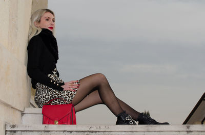 Side view of young woman sitting against sky