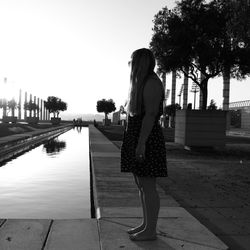 Side view of woman standing by reflecting pool against clear sky