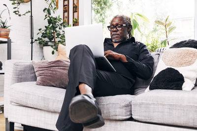 Senior male professional using laptop while sitting on sofa at home