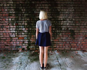 Rear view of girl standing against weathered brick wall in abandoned house