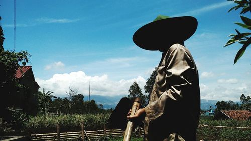 Side view of farmer standing on field against sky during sunny day