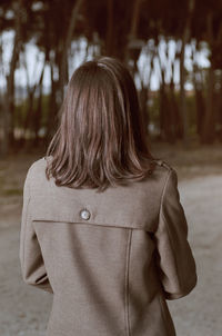 Rear view of woman wearing coat standing against trees on road