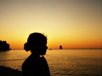Side view of silhouette teenage girl standing at beach against sky during sunset