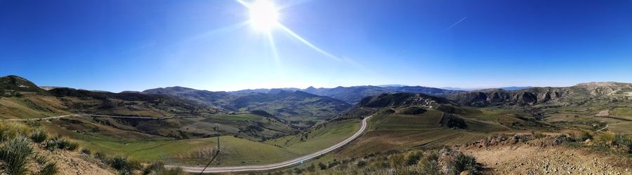 Panoramic view of mountains against blue sky on sunny day