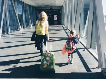 Rear view of mother pulling suitcase while walking with daughter at airport corridor