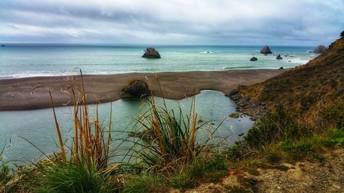 Scenic roadside overlook view of sea and foreground cliff against cloudy sky