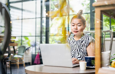 Young woman looking away while sitting on table at cafe