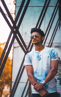 Young man wearing sunglasses standing against railing