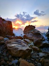 Rocks on beach against sky during sunset