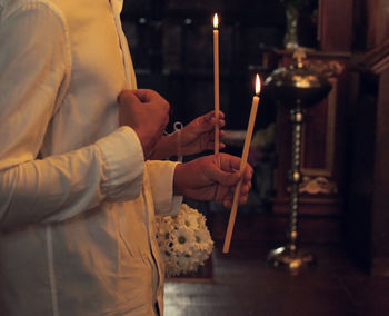 Midsection of man holding lit candles in temple