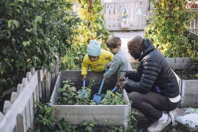 Side view of male teacher crouching near kids doing gardening at garden