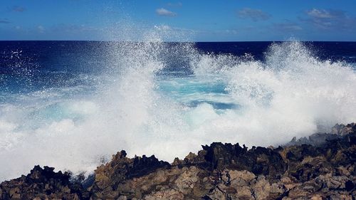 Waves splashing on rocks at shore against sky