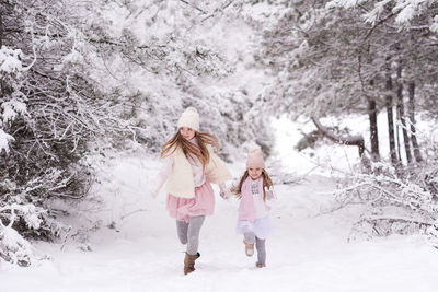 Full length of sisters holding hands walking on snow covered land