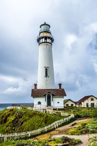 Lighthouse by building against sky