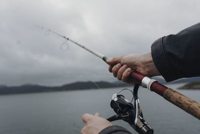 Man holding fishing rod by sea against sky