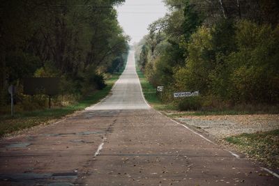 Empty road amidst trees against sky