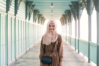 Portrait of smiling young woman wearing hijab standing on footbridge