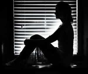 Woman sitting against window blinds at home