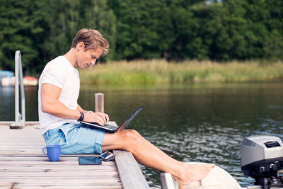 Full length side view of mature man using laptop on pier