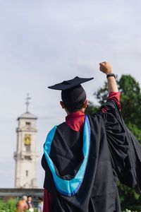 Rear view of man wearing black graduation gown against sky