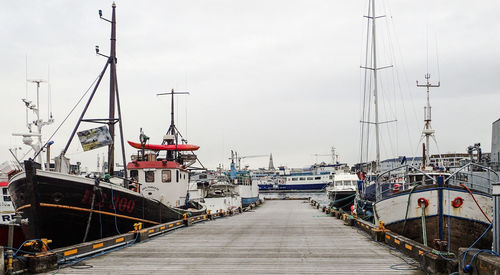 Fishing boats moored at harbor against sky