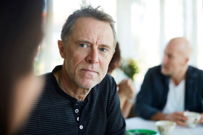 Mature man looking away with friends sitting in background at home